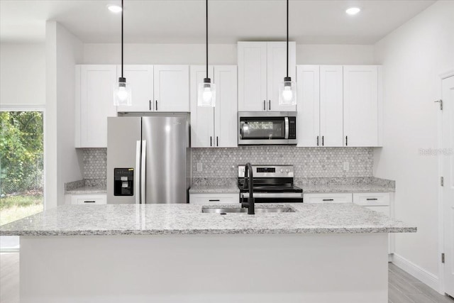 kitchen featuring a center island with sink, light stone counters, white cabinetry, and appliances with stainless steel finishes