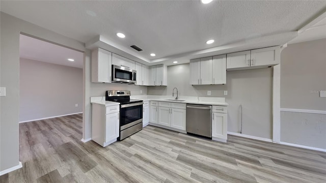 kitchen with light wood-type flooring, a textured ceiling, stainless steel appliances, sink, and white cabinets