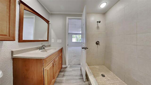 bathroom featuring a tile shower, vanity, a textured ceiling, crown molding, and wood-type flooring