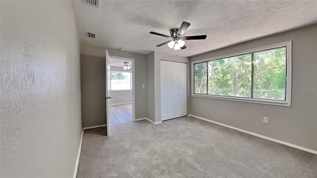 unfurnished bedroom featuring multiple windows, ceiling fan, a closet, and light colored carpet