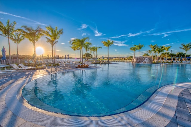 pool at dusk featuring a water view and a patio