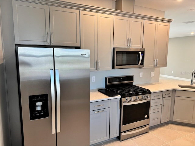 kitchen with gray cabinetry, sink, light tile patterned flooring, and appliances with stainless steel finishes