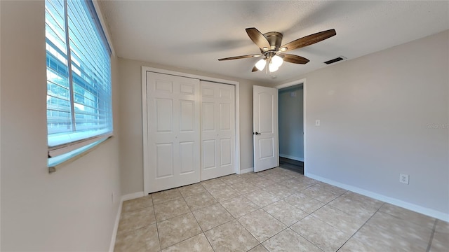 unfurnished bedroom featuring ceiling fan, light tile patterned flooring, a textured ceiling, and a closet