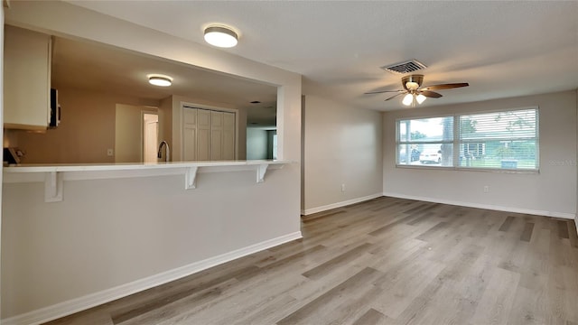 kitchen featuring ceiling fan, sink, kitchen peninsula, a breakfast bar, and light wood-type flooring