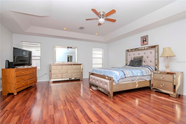 bedroom with ceiling fan, wood-type flooring, and a tray ceiling