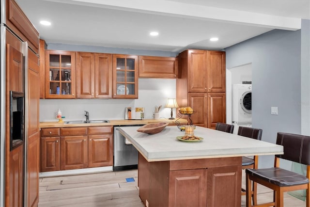 kitchen with a breakfast bar, sink, light wood-type flooring, stacked washing maching and dryer, and appliances with stainless steel finishes