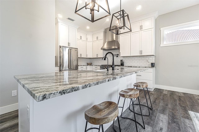 kitchen with wall chimney exhaust hood, high end fridge, white cabinetry, and decorative light fixtures