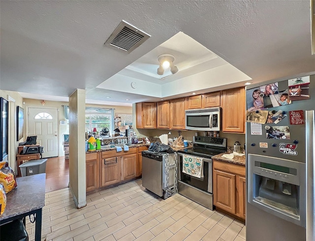 kitchen featuring light stone countertops, light wood-type flooring, stainless steel appliances, and a tray ceiling