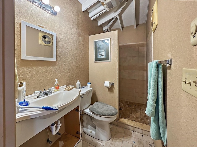 bathroom with tiled shower, tile patterned floors, sink, and toilet