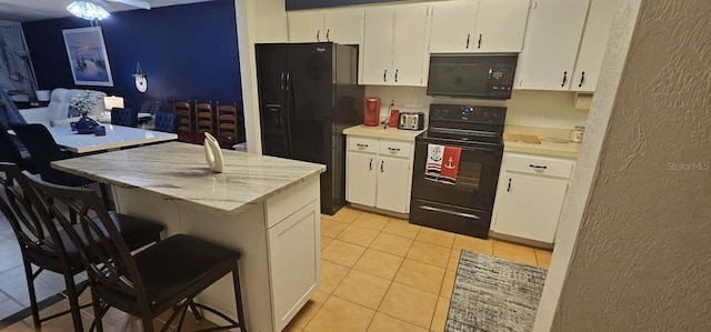 kitchen with light tile patterned floors, a breakfast bar, black appliances, light stone countertops, and white cabinets