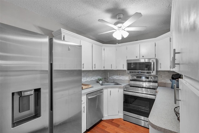 kitchen with stainless steel appliances, light countertops, light wood-style floors, white cabinetry, and a sink