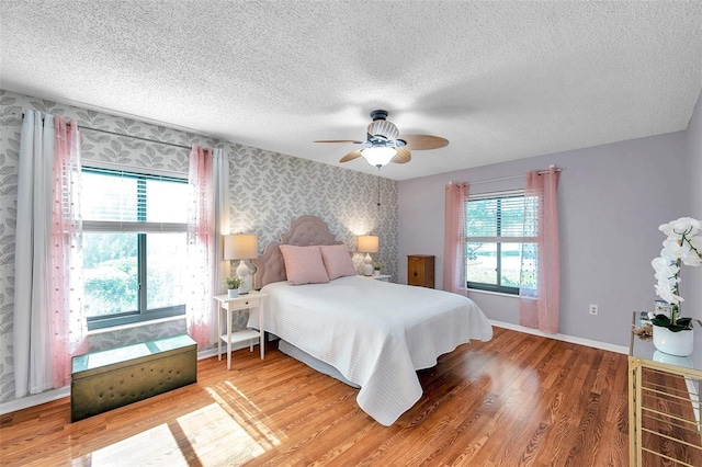 bedroom featuring a textured ceiling, a ceiling fan, baseboards, light wood-type flooring, and wallpapered walls