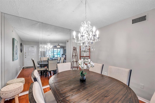 dining room featuring visible vents, a textured ceiling, wood finished floors, baseboards, and ceiling fan with notable chandelier