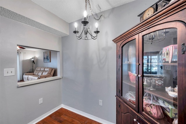 dining space with a chandelier, a textured ceiling, dark wood finished floors, and baseboards