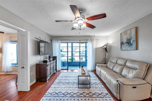 living room featuring ceiling fan, a textured ceiling, baseboards, and wood finished floors