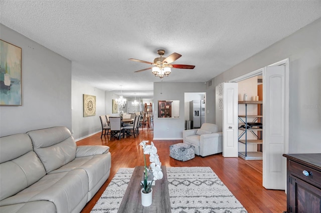 living room featuring a textured ceiling, baseboards, wood finished floors, and ceiling fan with notable chandelier