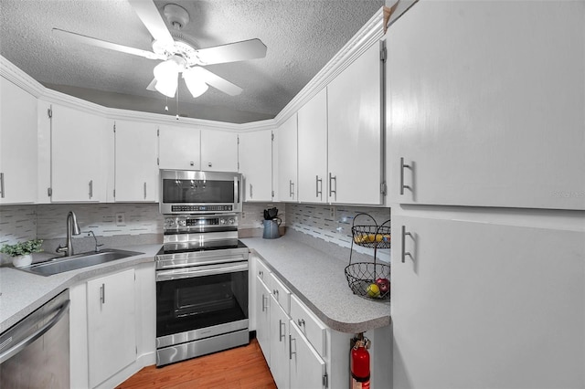 kitchen featuring decorative backsplash, appliances with stainless steel finishes, light wood-style floors, white cabinetry, and a sink