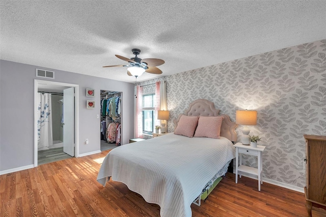 bedroom featuring wallpapered walls, baseboards, visible vents, a textured ceiling, and light wood-type flooring