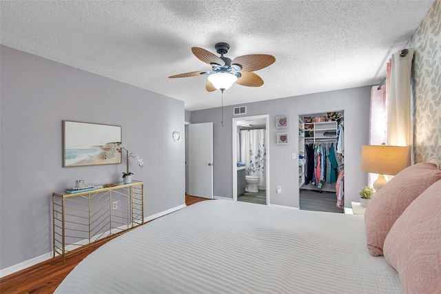 bedroom featuring a textured ceiling, wood finished floors, visible vents, baseboards, and a spacious closet