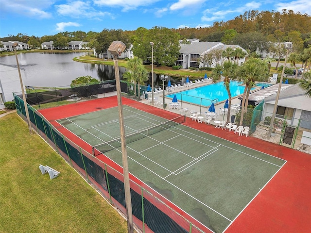 view of tennis court with a water view, fence, and a lawn