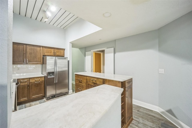 kitchen with a center island, rail lighting, tasteful backsplash, stainless steel fridge, and wood-type flooring