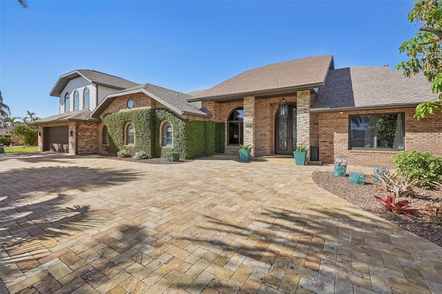 view of front of home with brick siding, decorative driveway, and a shingled roof