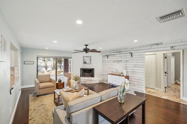 living room with recessed lighting, visible vents, a fireplace with raised hearth, a ceiling fan, and wood finished floors