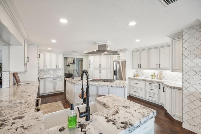 kitchen with light stone counters, dark wood-type flooring, a kitchen island with sink, stainless steel appliances, and ventilation hood