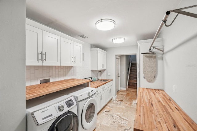 clothes washing area featuring cabinet space, visible vents, stone finish floor, washer and dryer, and a sink