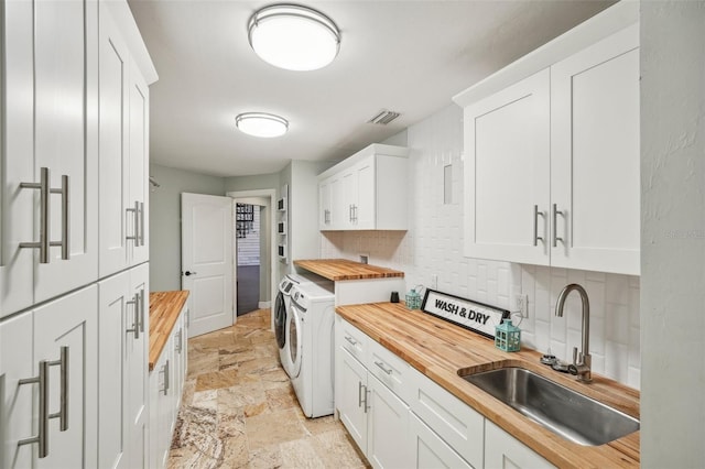 kitchen with stone tile floors, a sink, wood counters, visible vents, and washing machine and clothes dryer