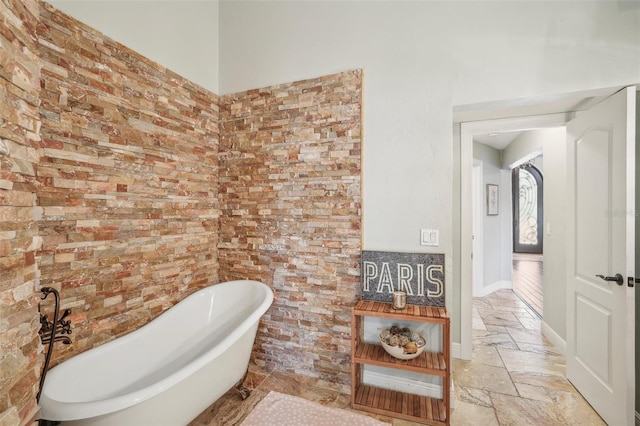 full bath featuring brick wall, a freestanding bath, baseboards, and stone tile flooring