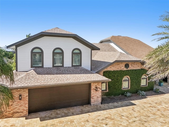 view of front of property with a shingled roof, decorative driveway, an attached garage, and brick siding