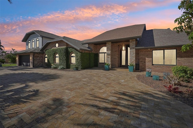 view of front of property with driveway, roof with shingles, a garage, and brick siding