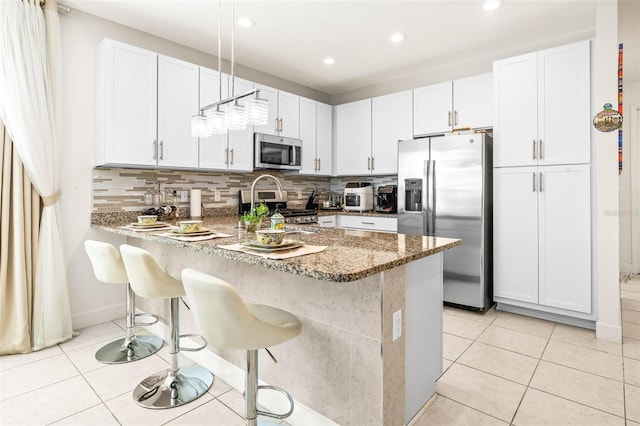 kitchen with pendant lighting, a kitchen breakfast bar, white cabinetry, and appliances with stainless steel finishes