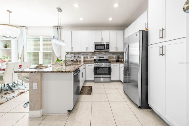 kitchen featuring white cabinetry, sink, dark stone counters, pendant lighting, and appliances with stainless steel finishes