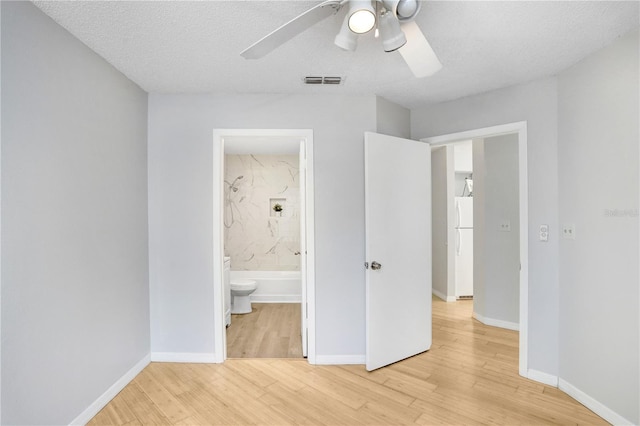 unfurnished bedroom featuring white refrigerator, ensuite bath, ceiling fan, a textured ceiling, and wood-type flooring