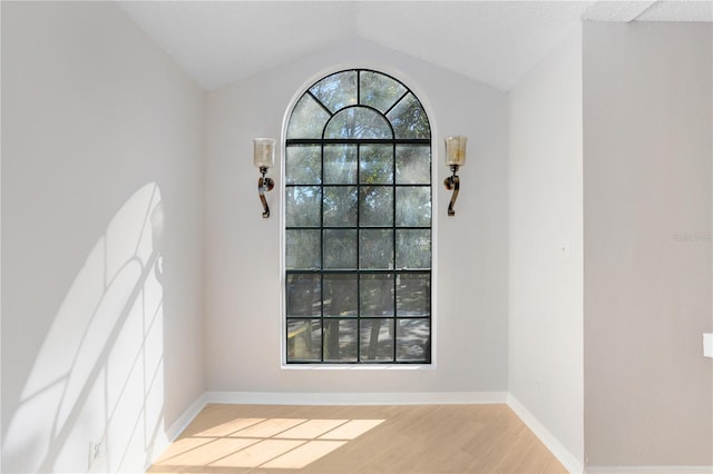 unfurnished dining area with a textured ceiling, vaulted ceiling, and light hardwood / wood-style flooring