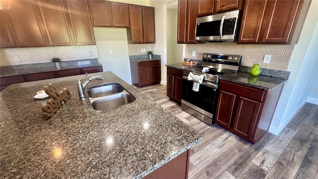 kitchen with backsplash, dark stone counters, a kitchen island with sink, light hardwood / wood-style flooring, and stainless steel appliances