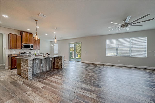 kitchen with an island with sink, wood-type flooring, decorative light fixtures, and appliances with stainless steel finishes