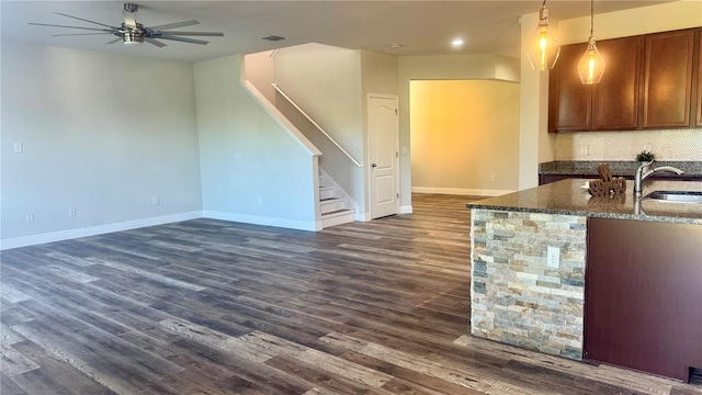 kitchen with dark stone counters, hanging light fixtures, dark hardwood / wood-style floors, ceiling fan, and decorative backsplash