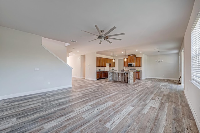 unfurnished living room with ceiling fan with notable chandelier and light hardwood / wood-style floors