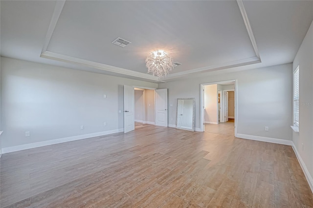 spare room featuring a tray ceiling, an inviting chandelier, and light wood-type flooring