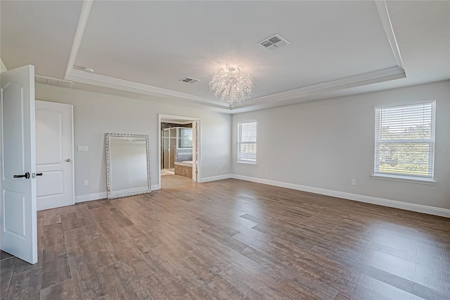 unfurnished bedroom with ensuite bathroom, wood-type flooring, and a tray ceiling