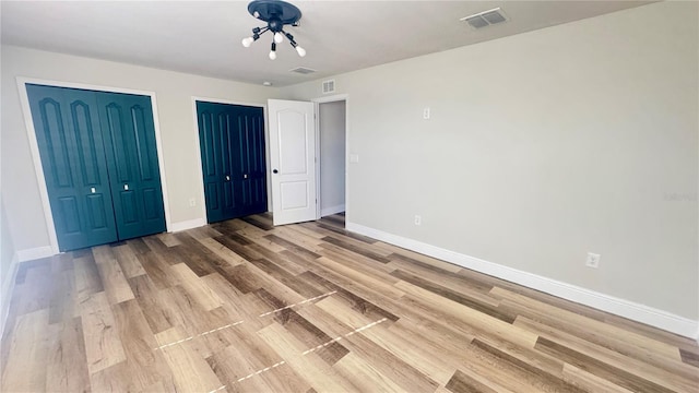 unfurnished bedroom with two closets and hardwood / wood-style flooring