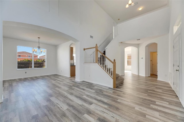 unfurnished living room with a towering ceiling, light hardwood / wood-style floors, and a notable chandelier