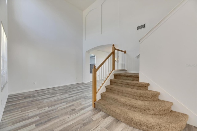 stairs with a towering ceiling and wood-type flooring