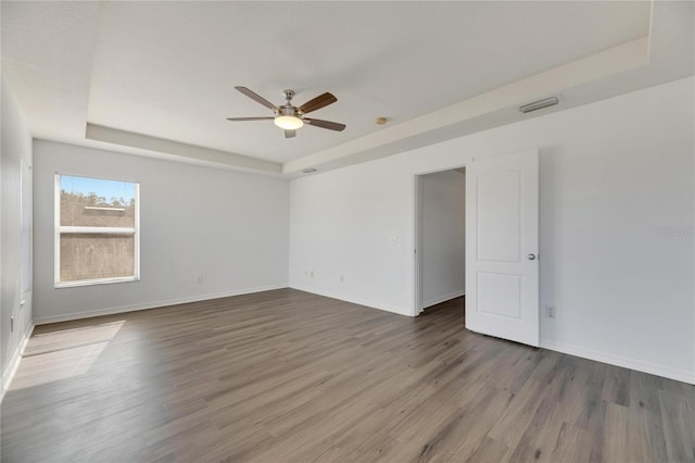 empty room featuring a raised ceiling, ceiling fan, and hardwood / wood-style flooring