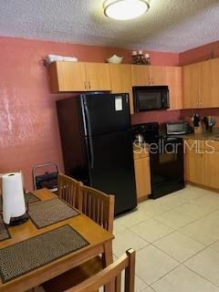 kitchen with light brown cabinetry, light tile patterned floors, black appliances, and a textured ceiling