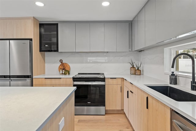 kitchen featuring stainless steel appliances, a sink, light countertops, light brown cabinetry, and modern cabinets