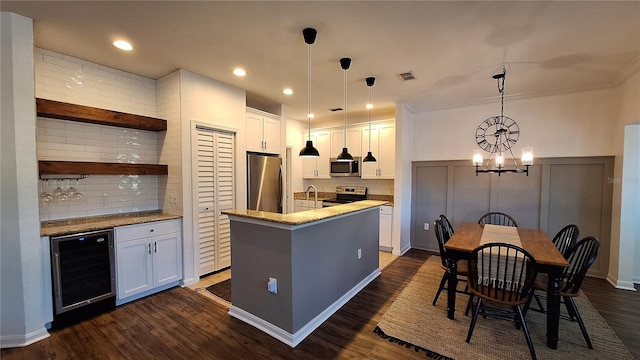 kitchen with white cabinets, hanging light fixtures, wine cooler, an island with sink, and appliances with stainless steel finishes